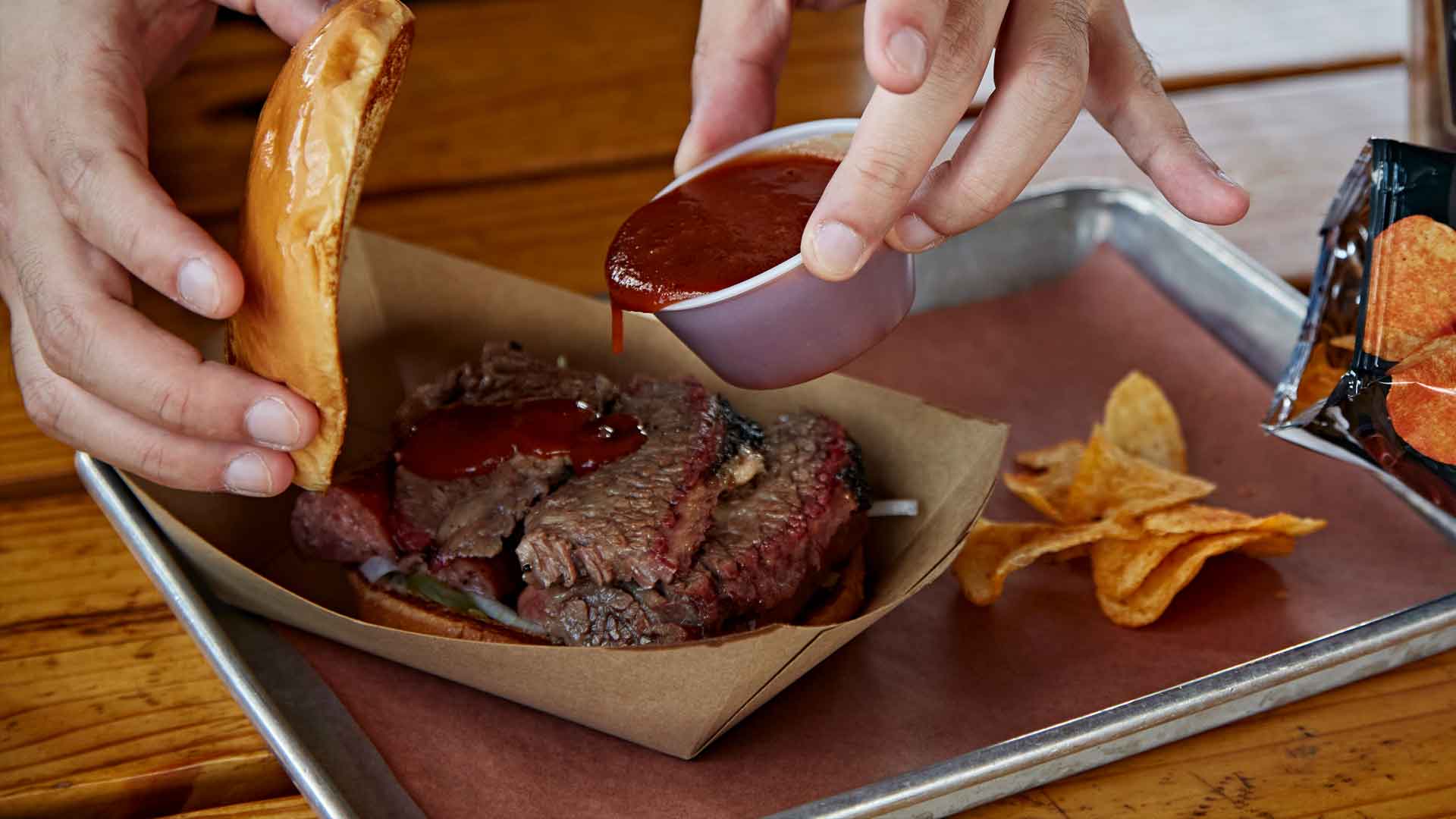 Close-up food photography of a perfectly smoked brisket BBQ sandwich being sauced